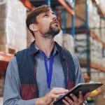 Un homme dans un entrepôt avec une tablette dans les mains, il travaille chez Somfy et regarde vers le haut
